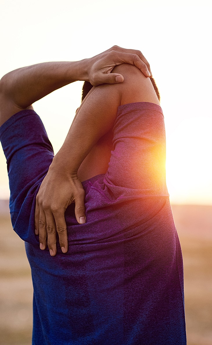Person stretching their arm at sunset.