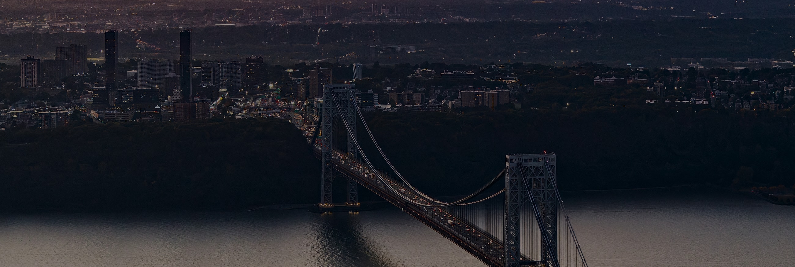 George Washington Bridge at dusk with city skyline.